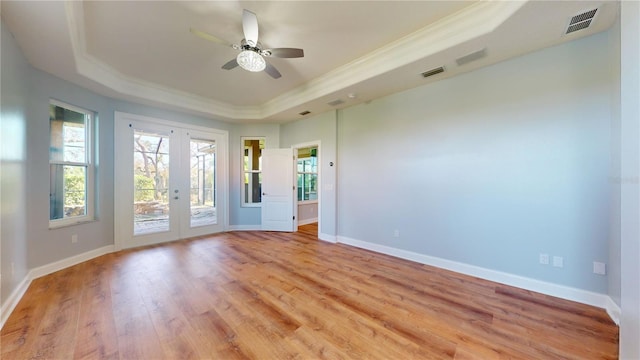 empty room with french doors, a tray ceiling, and light hardwood / wood-style floors