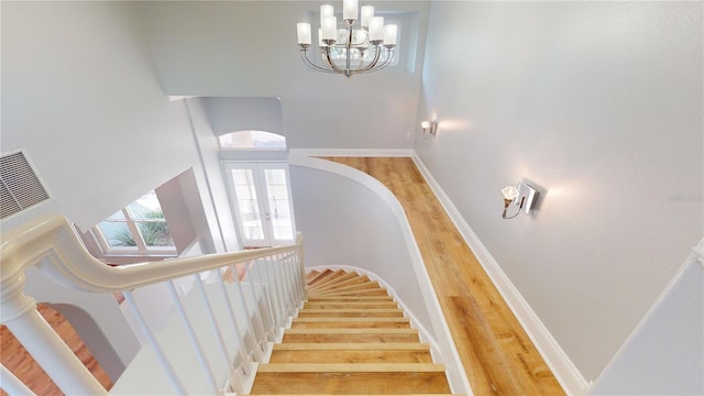 stairway featuring an inviting chandelier, french doors, and wood-type flooring