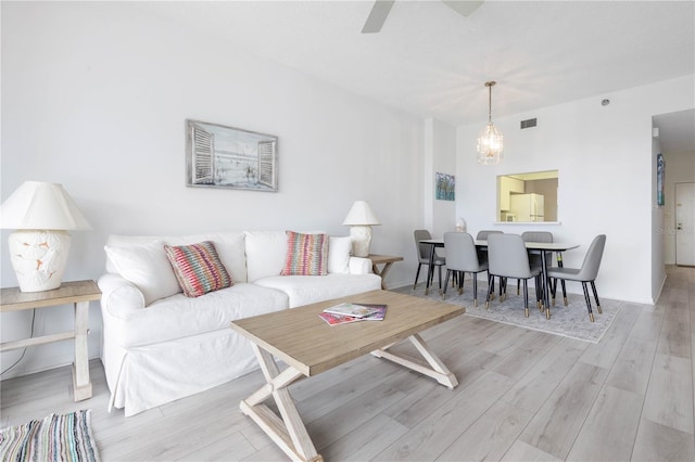 living room with ceiling fan with notable chandelier and light hardwood / wood-style floors