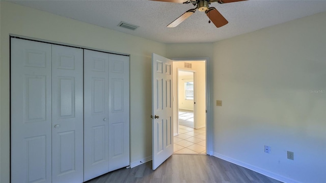 unfurnished bedroom featuring a closet, visible vents, a ceiling fan, a textured ceiling, and wood finished floors