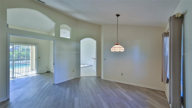 spare room featuring baseboards, arched walkways, lofted ceiling, wood finished floors, and a textured ceiling