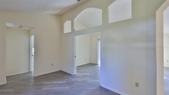 empty room featuring high vaulted ceiling, baseboards, and wood finished floors