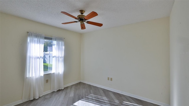 empty room with a textured ceiling, wood finished floors, a ceiling fan, and baseboards