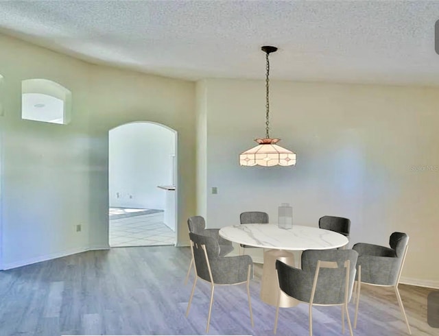 dining area featuring baseboards, a textured ceiling, arched walkways, and wood finished floors