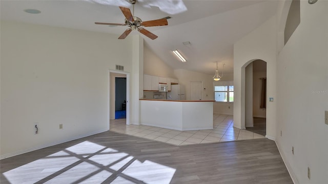 interior space featuring arched walkways, high vaulted ceiling, visible vents, a ceiling fan, and light wood finished floors