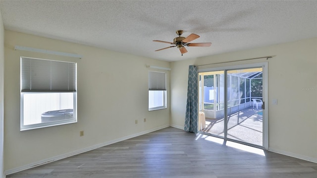 empty room with a ceiling fan, a sunroom, a textured ceiling, and wood finished floors