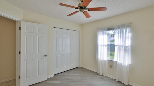 unfurnished bedroom featuring a closet, a textured ceiling, baseboards, and wood finished floors