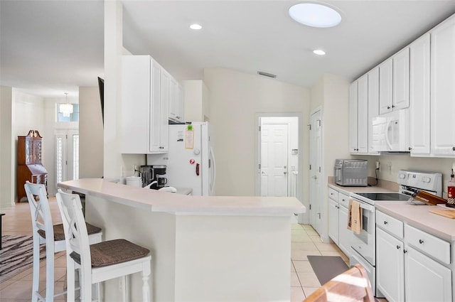 kitchen featuring a breakfast bar, vaulted ceiling, light tile patterned flooring, white cabinetry, and white appliances