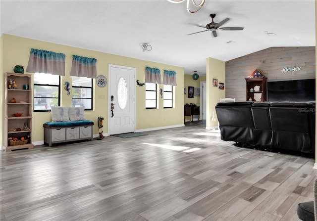 living room featuring light wood-type flooring, wooden walls, vaulted ceiling, and ceiling fan