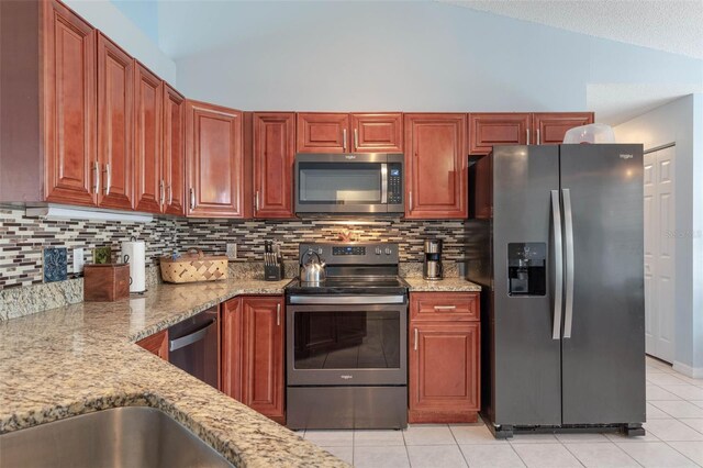 kitchen featuring stainless steel appliances, lofted ceiling, light stone counters, tasteful backsplash, and light tile patterned flooring