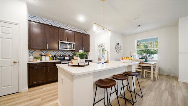 kitchen featuring light wood-type flooring, appliances with stainless steel finishes, pendant lighting, sink, and an island with sink