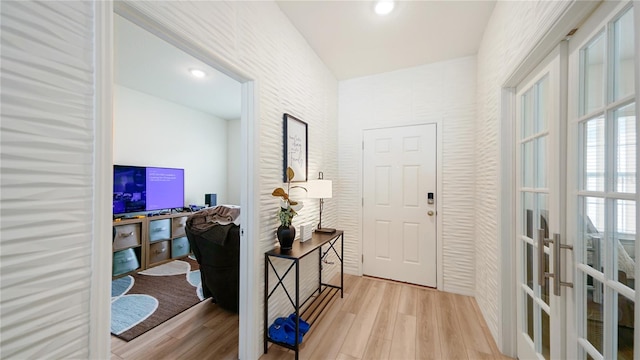 corridor with light wood-type flooring, french doors, and brick wall