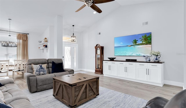 living room featuring ceiling fan with notable chandelier, plenty of natural light, light hardwood / wood-style floors, and vaulted ceiling