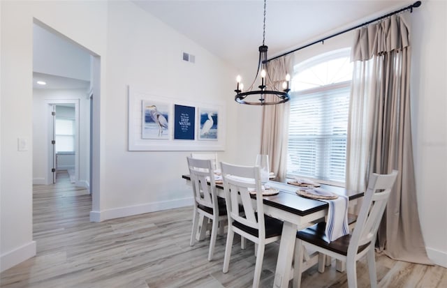 dining area featuring a chandelier, vaulted ceiling, light wood finished floors, and baseboards