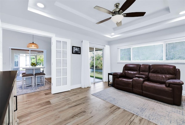 living room featuring ceiling fan, a raised ceiling, light hardwood / wood-style flooring, and french doors