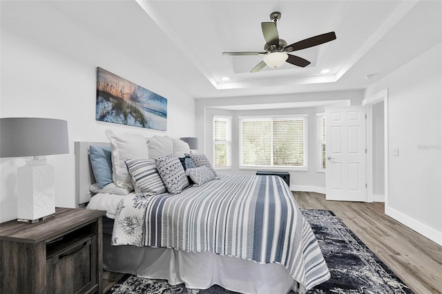 bedroom featuring ceiling fan, a raised ceiling, and light wood-type flooring