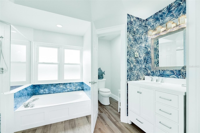 bathroom featuring wallpapered walls, toilet, wood finished floors, a garden tub, and vanity