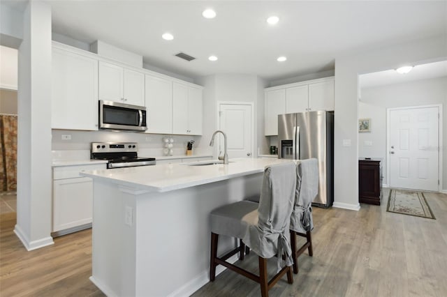 kitchen featuring stainless steel appliances, white cabinetry, sink, an island with sink, and light wood-type flooring