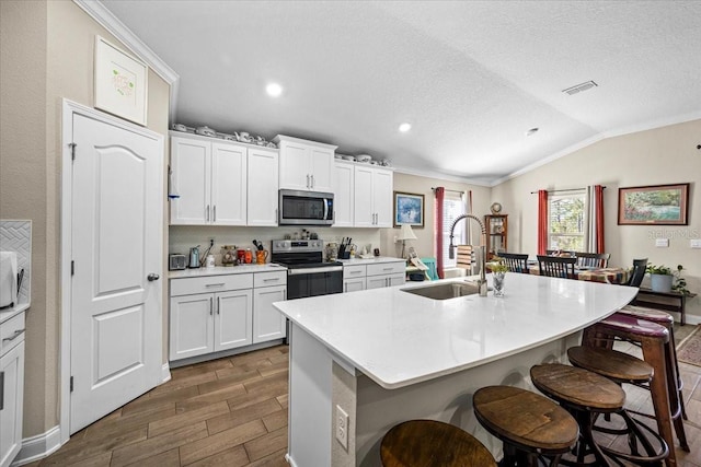 kitchen featuring stainless steel appliances, a center island with sink, sink, and vaulted ceiling