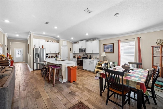 dining room featuring sink, light wood-type flooring, a textured ceiling, vaulted ceiling, and ornamental molding