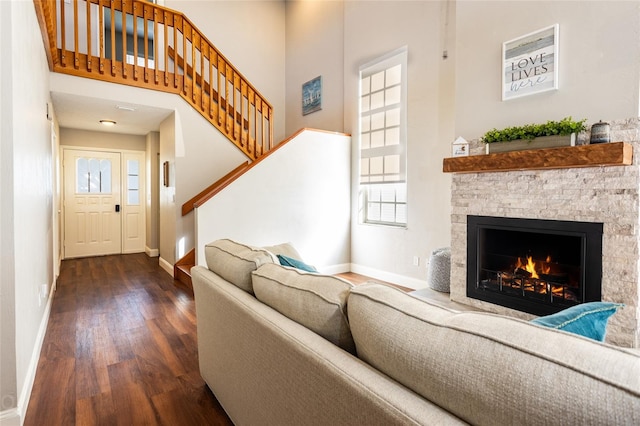 living room with a stone fireplace, a towering ceiling, and dark hardwood / wood-style flooring