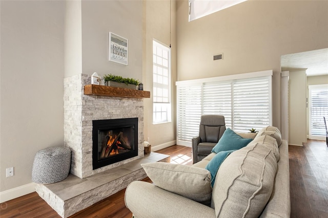 living room with a stone fireplace, wood-type flooring, and a high ceiling