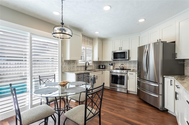 kitchen with dark hardwood / wood-style flooring, white cabinets, hanging light fixtures, light stone countertops, and appliances with stainless steel finishes