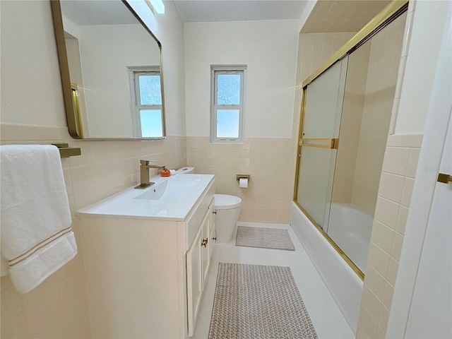 full bathroom featuring combined bath / shower with glass door, vanity, tile walls, tile patterned flooring, and toilet