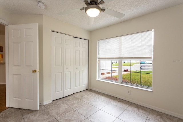 unfurnished bedroom with light tile patterned floors, ceiling fan, a textured ceiling, and a closet