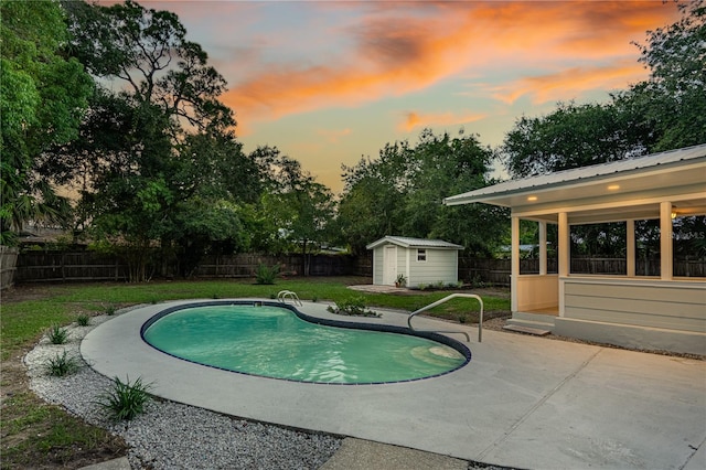 pool at dusk with a patio area, a lawn, and a shed