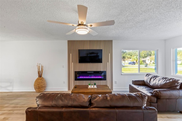 living room with a large fireplace, ceiling fan, light hardwood / wood-style floors, and a textured ceiling