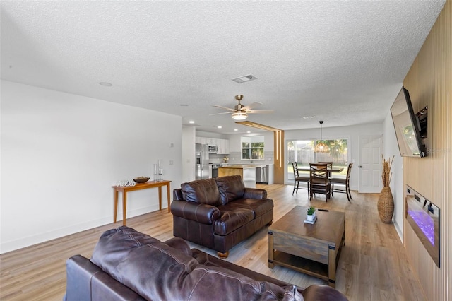 living room with a textured ceiling, light hardwood / wood-style flooring, and ceiling fan