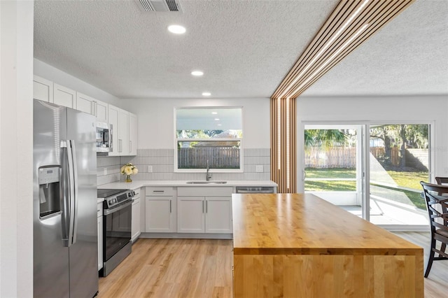 kitchen featuring backsplash, white cabinets, sink, light hardwood / wood-style flooring, and appliances with stainless steel finishes