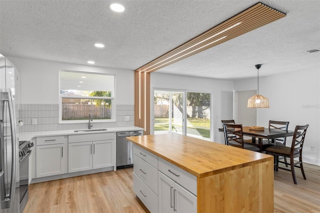 kitchen with wooden counters, stainless steel appliances, sink, a center island, and white cabinetry