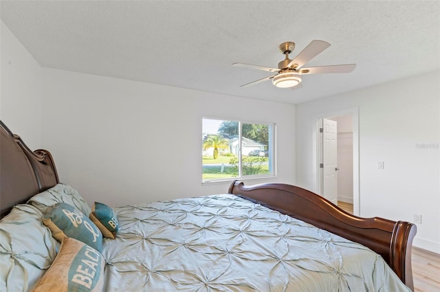 bedroom featuring ceiling fan, a spacious closet, a textured ceiling, light hardwood / wood-style floors, and a closet