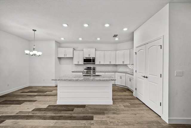 kitchen with white cabinetry, light stone counters, a center island with sink, and stainless steel appliances