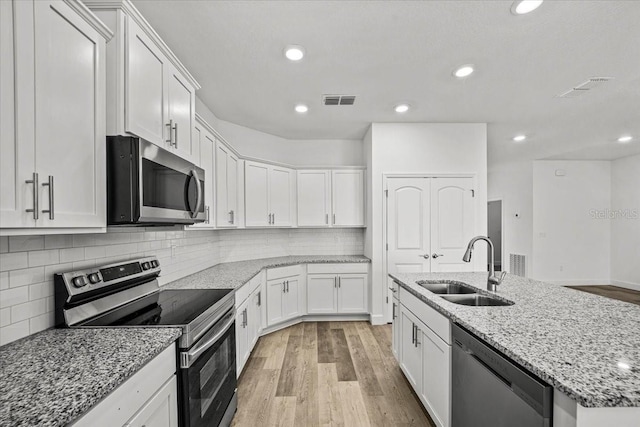 kitchen with light stone counters, light wood-type flooring, appliances with stainless steel finishes, sink, and white cabinets