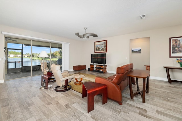 living room featuring light wood-type flooring, a water view, baseboards, and visible vents