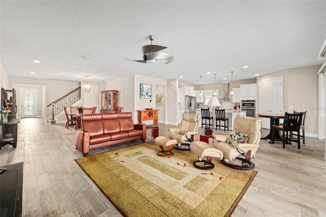 living area featuring light wood finished floors, recessed lighting, a textured ceiling, baseboards, and stairs