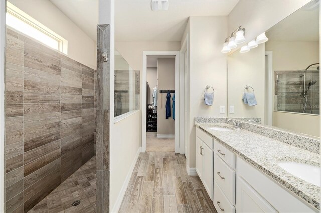 full bathroom with double vanity, a spacious closet, a sink, wood finished floors, and a walk in shower