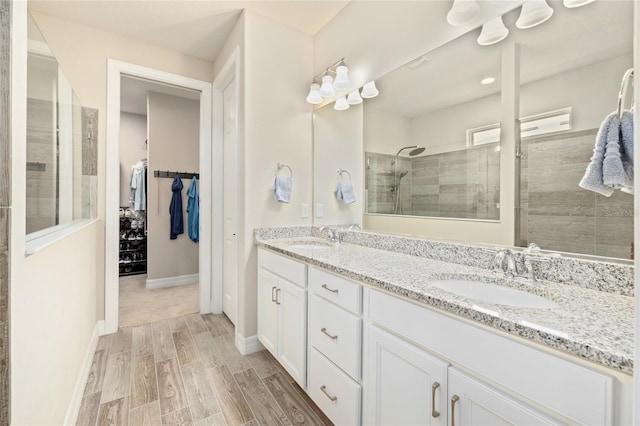 bathroom featuring wood finished floors, double vanity, a sink, and a walk in shower