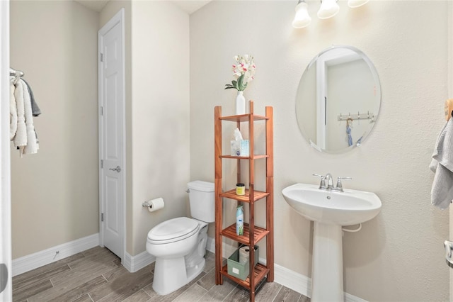 half bath featuring baseboards, a sink, toilet, and wood tiled floor