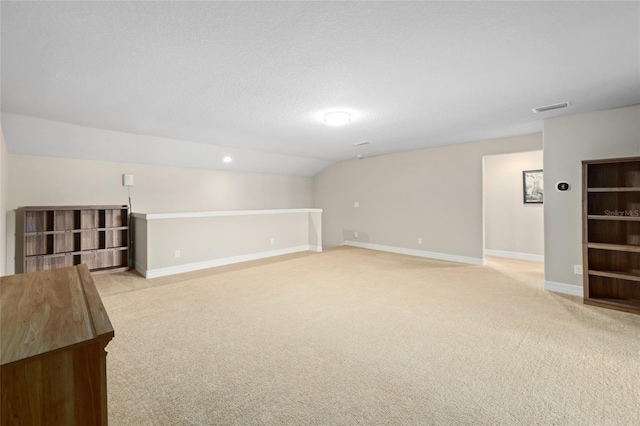 interior space with visible vents, light carpet, vaulted ceiling, a textured ceiling, and baseboards