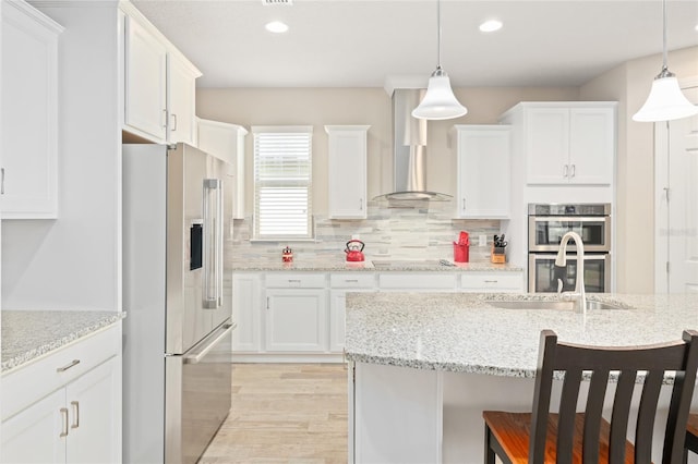 kitchen featuring a breakfast bar area, stainless steel appliances, a sink, white cabinets, and wall chimney range hood