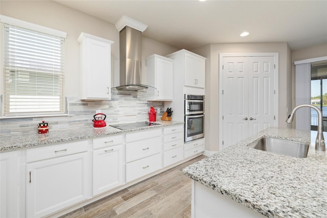 kitchen with wall chimney exhaust hood, black electric cooktop, stainless steel double oven, white cabinetry, and a sink