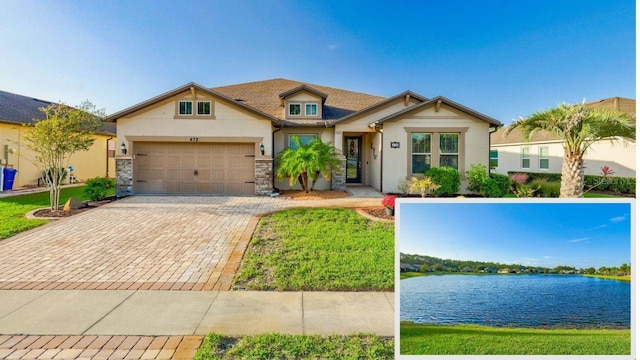 view of front of house featuring an attached garage, a water view, stone siding, decorative driveway, and stucco siding