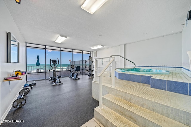 exercise room with a water view, a textured ceiling, and floor to ceiling windows