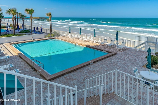 view of swimming pool with a view of the beach, a water view, and a patio