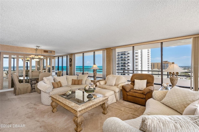 living room with a textured ceiling, floor to ceiling windows, a water view, a chandelier, and light colored carpet