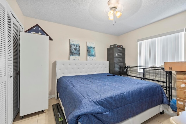 bedroom featuring a textured ceiling, a closet, ceiling fan, and light tile patterned flooring